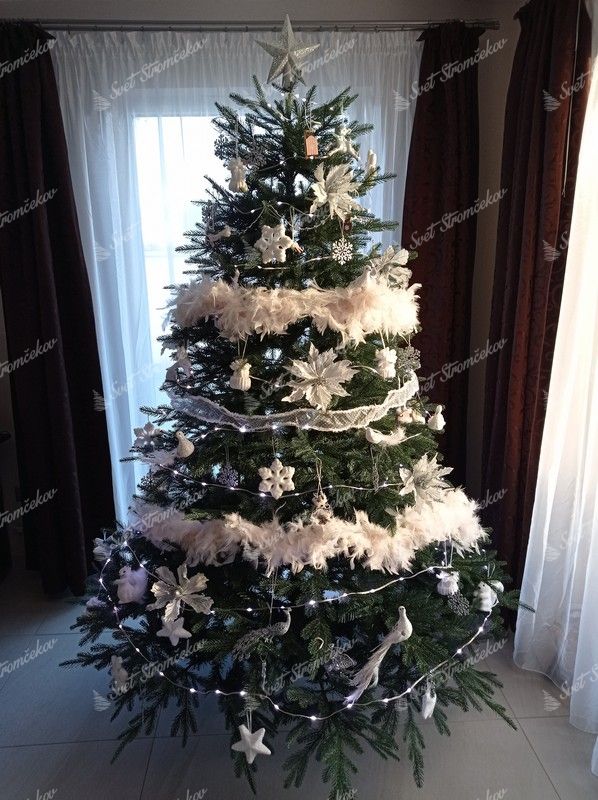 Široký umelý vianočný stromček so zelenými vetvičkami, ozdobený bielymi ozdobami.