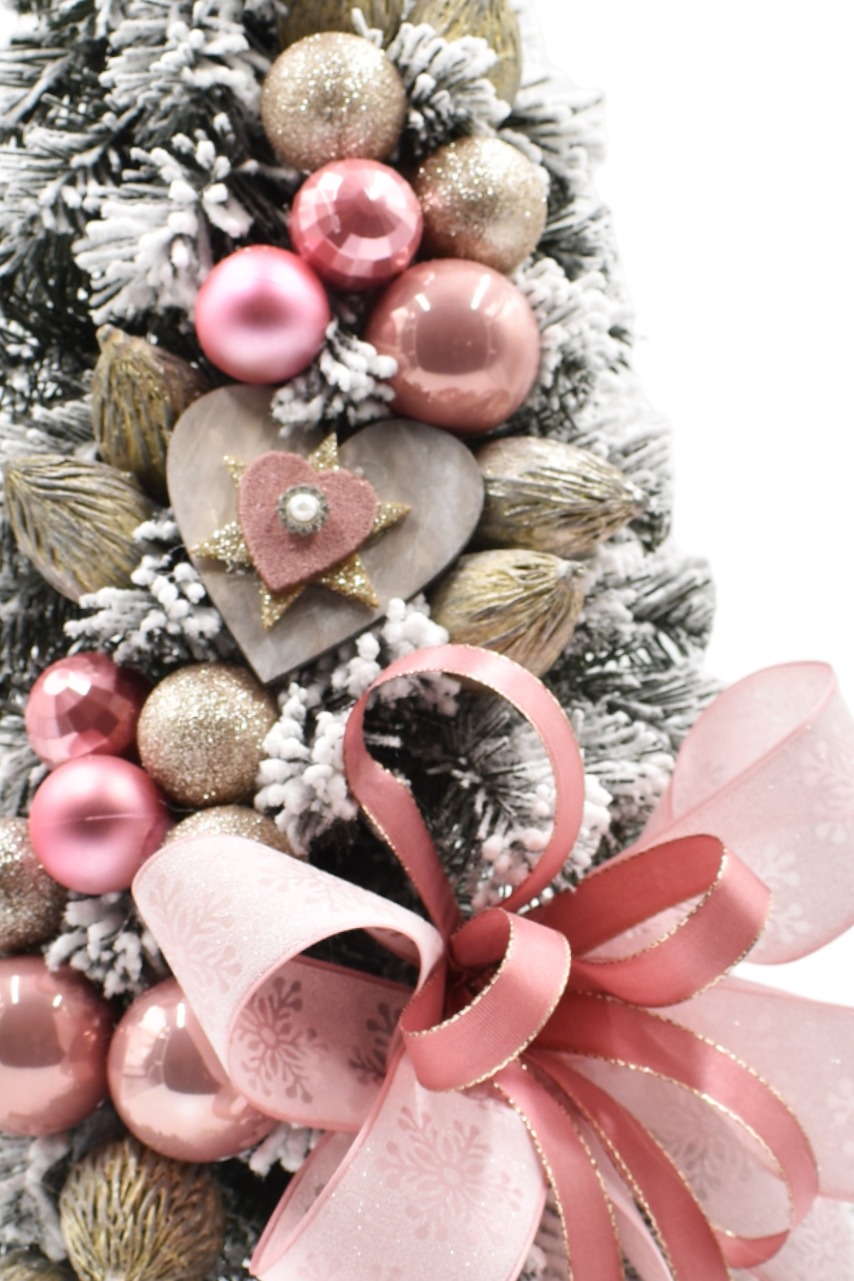 Zasnežený malý vianočný stromček s ružovými vianočnými guľami a mašľou.